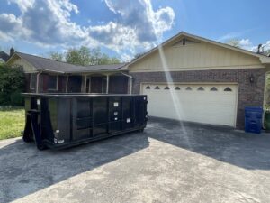A black dumpster placed in a residential driveway by Beetles Dumpsters Rental & Junk Removal in Huntsville, AL.