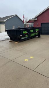 A black dumpster from Waste-Away Dumpsters & Disposal LLC placed in a residential driveway in Sioux Falls, SD.