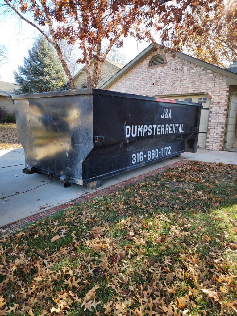 A black J & A Haul Away & Dumpster Rentals dumpster on a residential driveway in Derby, KS.