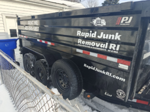 A black dumpster trailer from Dumpsters RI.com - Dumpster Rentals RI parked in a residential driveway in Rhode Island.