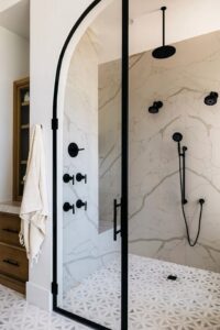 A modern bathroom shower with black fixtures, marble-look tiles, and an arched glass door, installed by Rapid Restoration and Construction in Mesa, AZ.