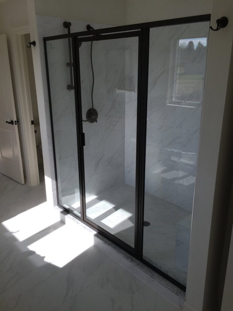 Black-framed sliding shower doors complementing marble-look tiled walls in a bathroom project by Lehigh Shower Glass in Bethlehem, PA