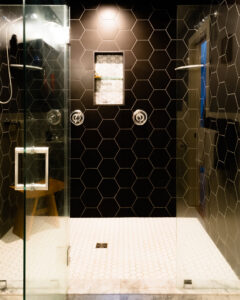 A modern walk-in shower featuring black hexagonal wall tiles and white hexagonal floor tiles, installed by Boyd's Custom Building in Charlotte, NC.