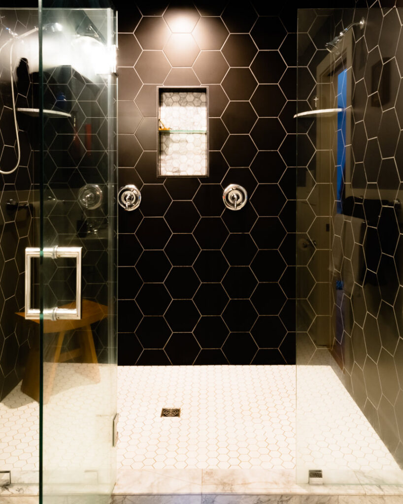 A modern walk-in shower featuring black hexagonal wall tiles and white hexagonal floor tiles, installed by Boyd's Custom Building in Charlotte, NC.