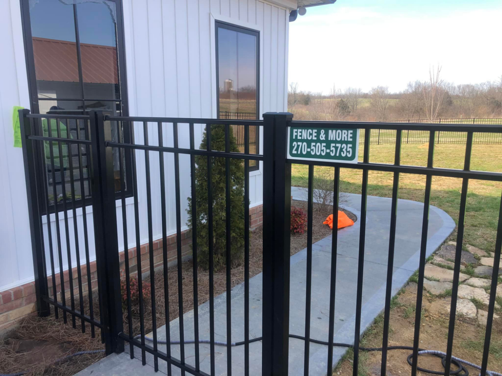 A close-up of a black metal fence gate with a Fence & More sign, installed in Elizabethtown, KY