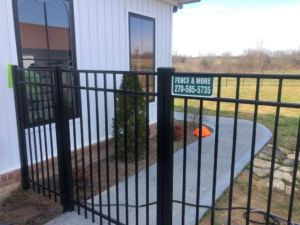 A close-up of a black metal fence gate with a Fence & More sign, installed in Elizabethtown, KY