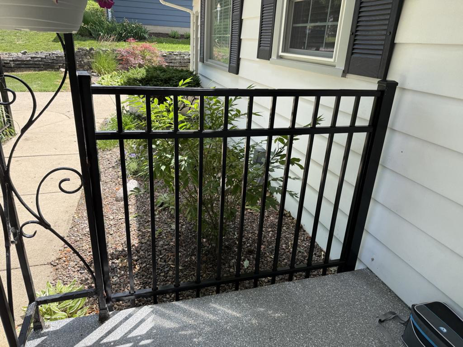 A section of black metal fence installed next to a house porch by A to Z Quality Fencing and Structures-Appleton, WI.