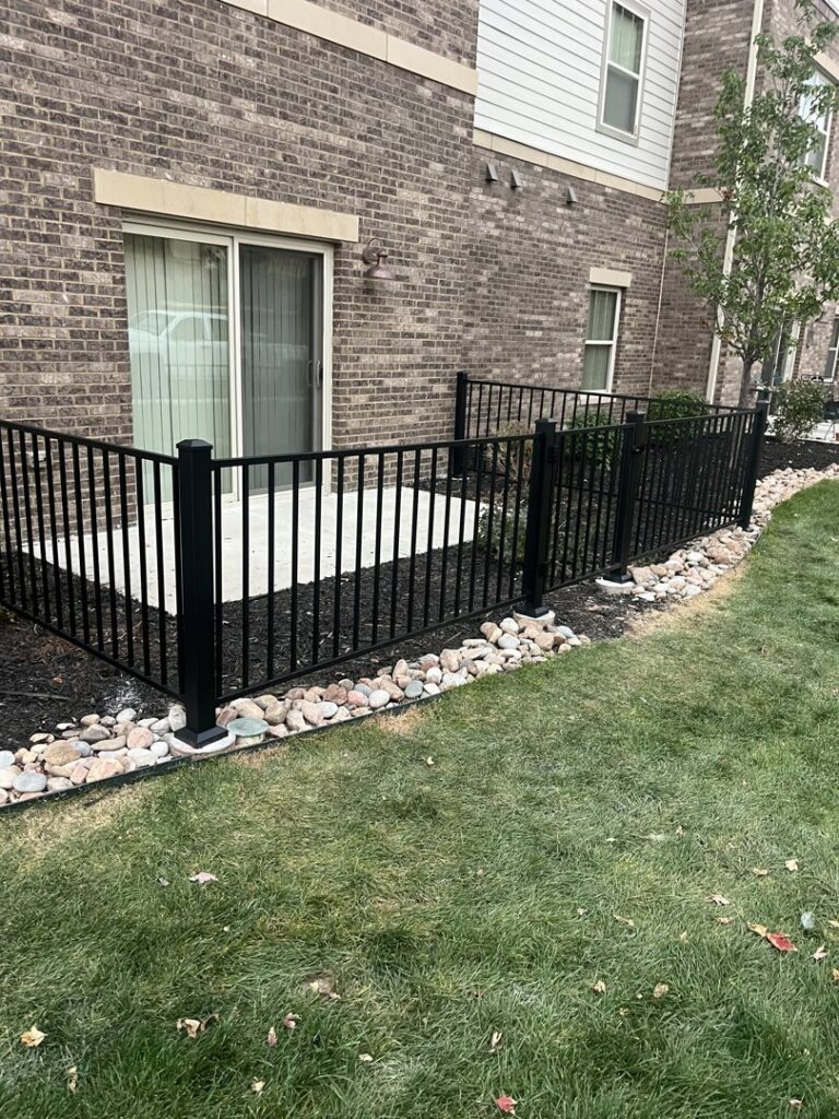 A newly installed black metal fence enclosing a patio area by Blue Collar Service Pros in Aurora, CO.
