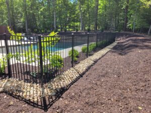 A newly installed black metal fence around a swimming pool with decorative rocks by Minors Fences in Ashland, VA.