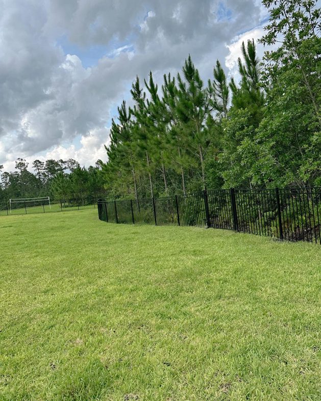 A durable black metal security fence installed around a large grassy field by LV Fence and Gates in Jacksonville, FL.