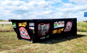 A large black roll-off dumpster from Affordable Dumpster's LLC sits on a grassy field in Springfield, MO, ready for junk removal.