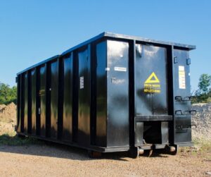 A large black Delta Waste Solutions roll-off dumpster on a gravel lot, available for junk removal projects in Hattiesburg, MS.
