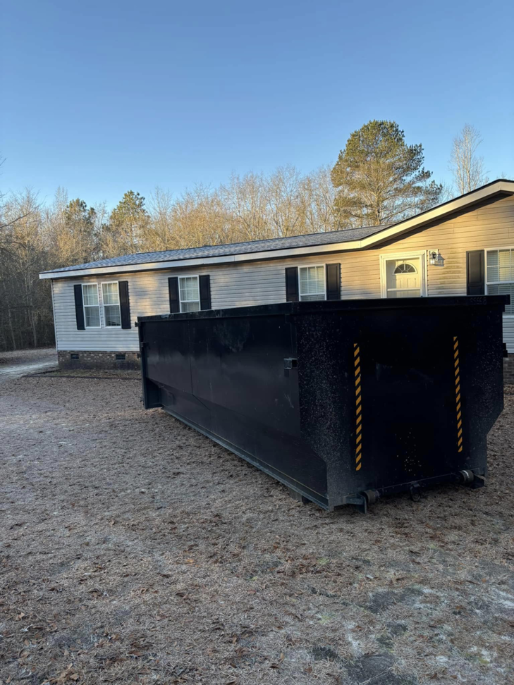 A black roll-off dumpster placed at a residential property for junk removal by BRR services in Fayetteville, NC