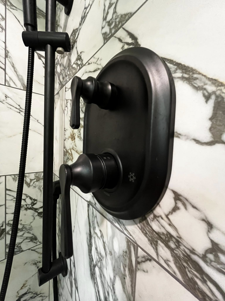 A modern black shower fixture expertly installed on elegant marble-look tiles by Simko Tile & Bath in Macon, GA.