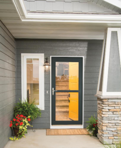 A stylish black storm door installed on a gray house with a vibrant yellow main door by Denver Storm Door in Denver, CO.