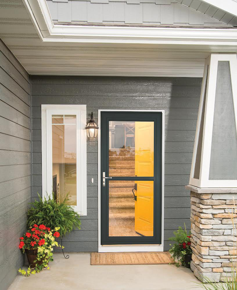 A stylish black storm door installed on a gray house with a vibrant yellow main door by Denver Storm Door in Denver, CO.