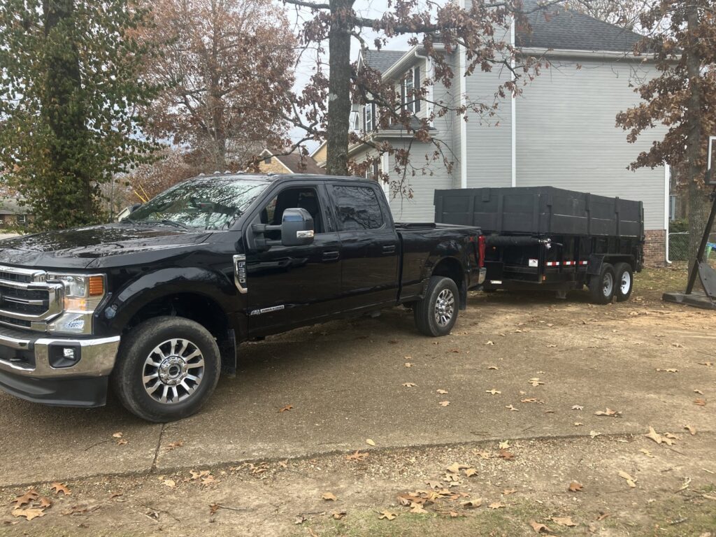 A black pickup truck towing an empty dump trailer from Mobile Dumpster Solutions on a residential driveway in Chattanooga, TN.