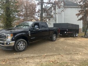 A black pickup truck towing an empty dump trailer from Mobile Dumpster Solutions on a residential driveway in Chattanooga, TN.