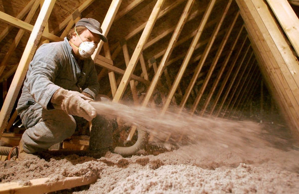 A professional installing blown-in attic insulation for a home by Blown Rite Insulation and Gutters in Wilmington, NC.