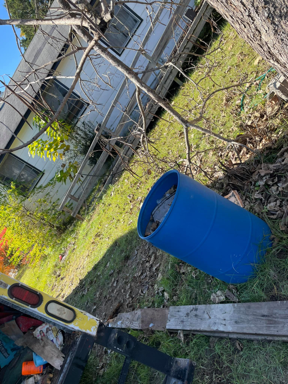 A blue barrel filled with junk and debris next to a removal truck, handled by Ty's touch junk removal,LLC in Fayetteville, NC.
