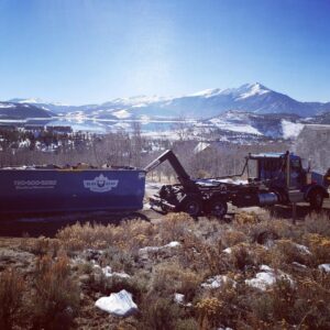 A Blue Bear Waste Services truck with a dumpster in a scenic mountainous area near Denver, CO.