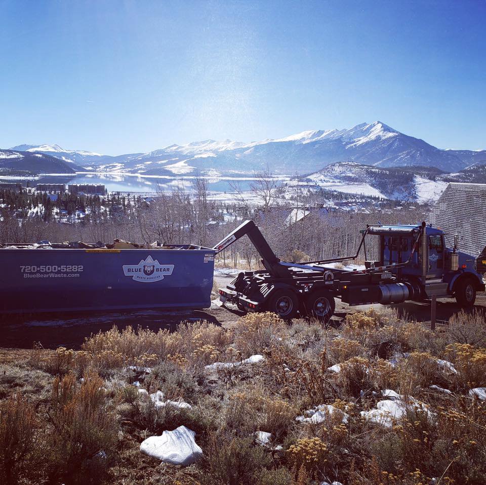A Blue Bear Waste Services truck with a dumpster in a scenic mountainous area near Denver, CO.
