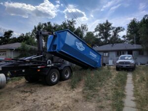 A Blue Bear Waste Services truck picking up a roll-off dumpster from a residential property in Denver, CO.