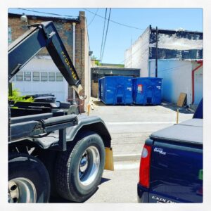 A Blue Bear Waste Services truck with two dumpsters in an urban alleyway in Denver, CO.