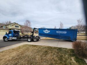 A Blue Bear Waste Services truck placing a roll-off dumpster in a residential neighborhood in Denver, CO.