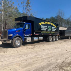 A blue dump truck with the Central Georgia Tree Service logo and a trailer on a dirt road in Macon, GA
