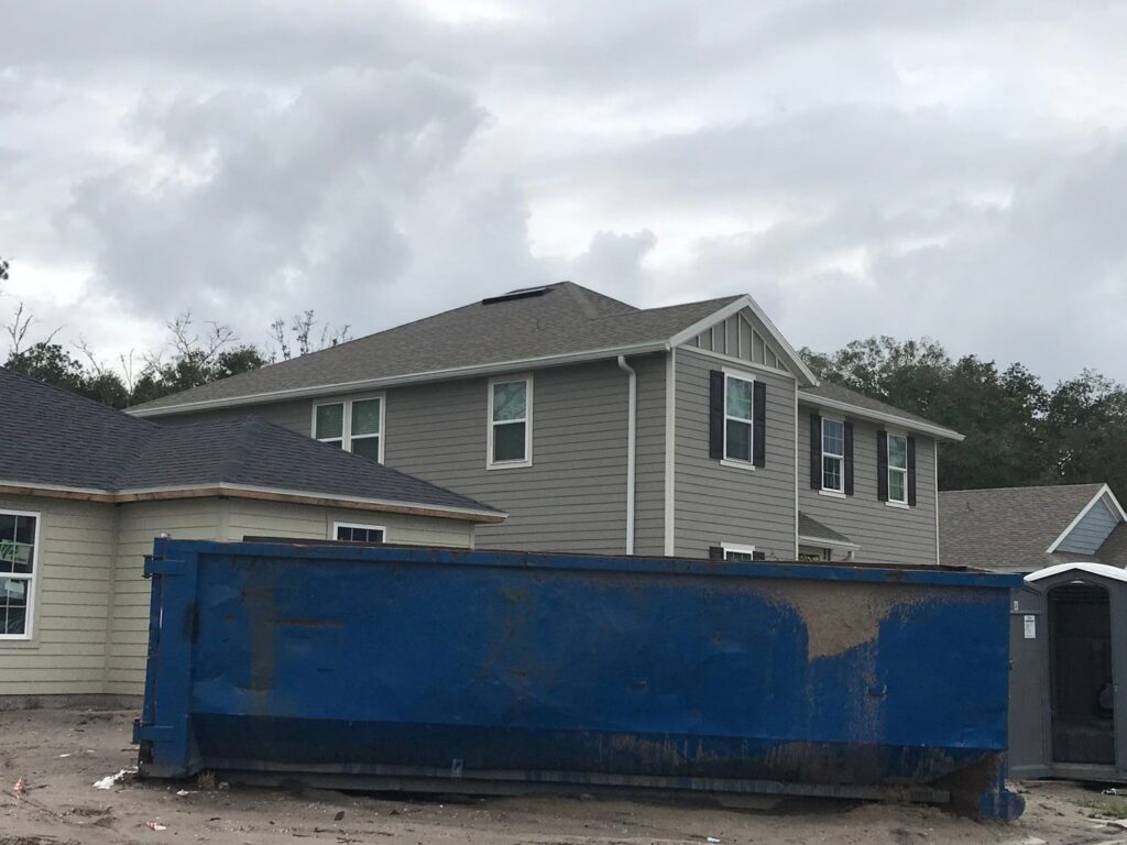 A blue roll-off dumpster, partially filled with debris, placed at a new construction site by Waste Master Dumpster Rental Orlando, FL.