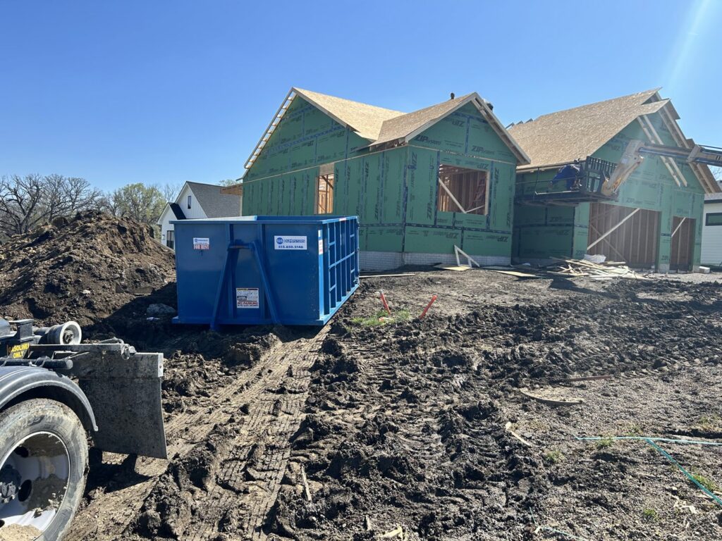 A blue dumpster from 515 Dumpsters at a construction site with a truck in West Des Moines, IA.