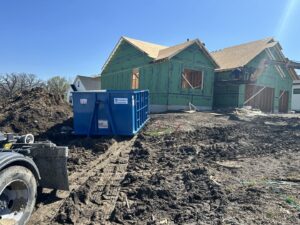 A blue dumpster from 515 Dumpsters at a construction site with a truck in West Des Moines, IA.
