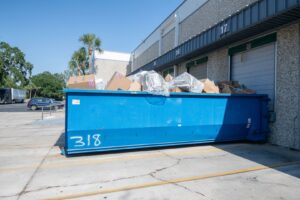 A blue roll-off dumpster filled with cardboard boxes and general debris outside a commercial building by Waste Master Dumpster Rental Orlando, FL.