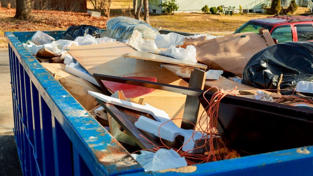 A blue roll-off dumpster filled with a mix of household junk and construction debris, ready for removal in Sterling Heights, MI.