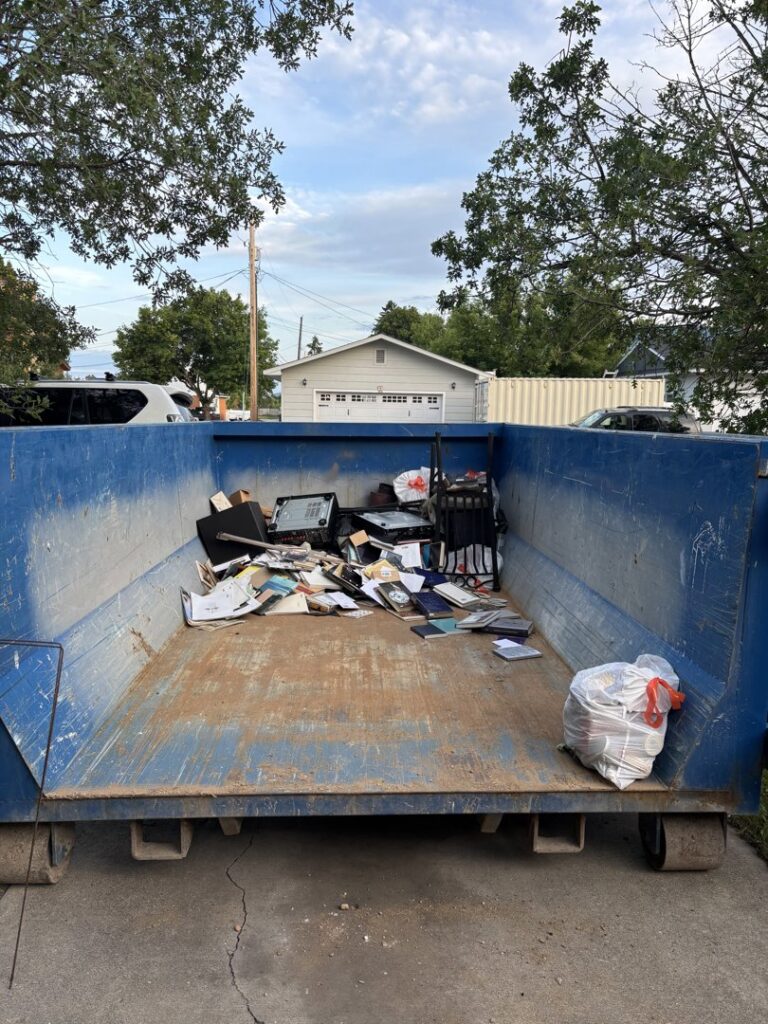 A blue roll-off dumpster partially filled with office junk, ready for removal by Evergreen Disposal in Kalispell, MT.