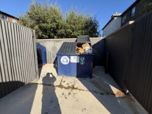 A blue dumpster filled with cardboard boxes and other debris, ready for collection by Junk Out Boyz LLC in Georgetown, TX.