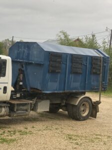 A blue roll-off dumpster loaded onto a NID Dumpster Rental truck, ready for transport in Nashua, IA.