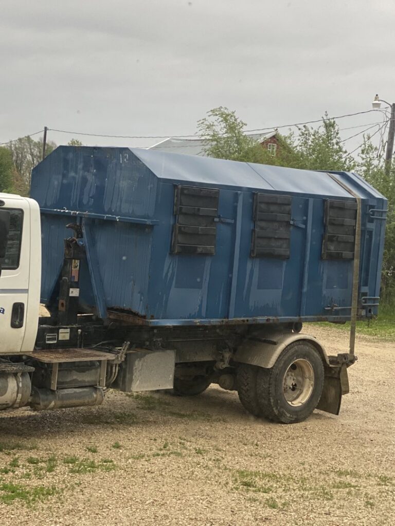 A blue roll-off dumpster loaded onto a NID Dumpster Rental truck, ready for transport in Nashua, IA.