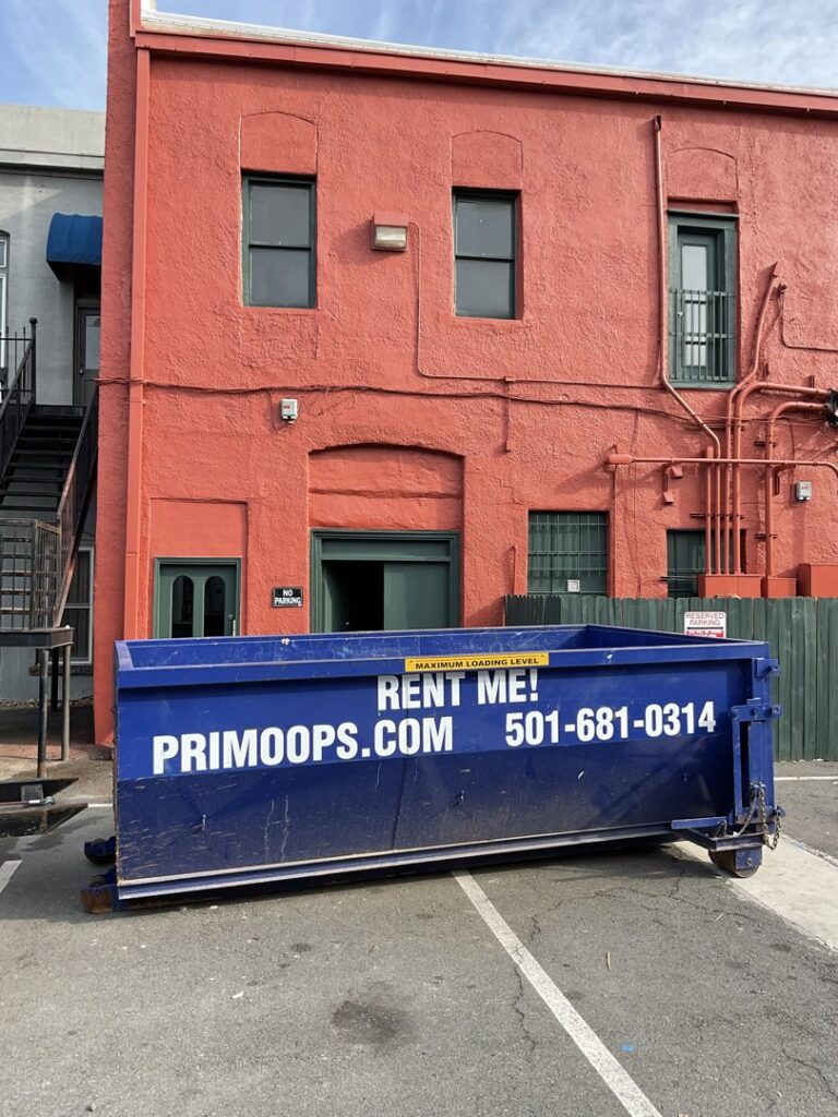 A blue dumpster from Primo Operations, available for rental, parked in front of a building in North Little Rock, AR.