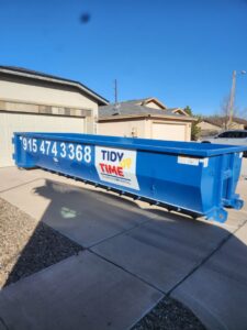 A blue Tidy up time dumpster placed in a residential driveway for junk removal services in El Paso, TX.