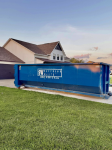 A blue dumpster from Superior Waste Management placed in front of a residential home for junk removal in Amory, MS.