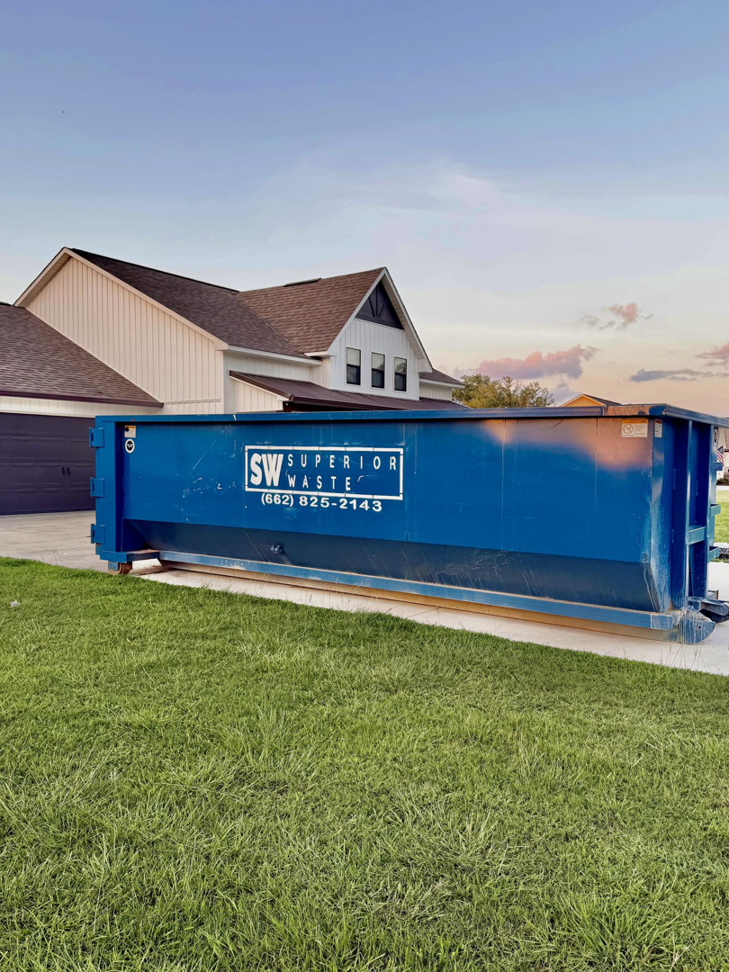 A blue dumpster from Superior Waste Management placed in front of a residential home for junk removal in Amory, MS.