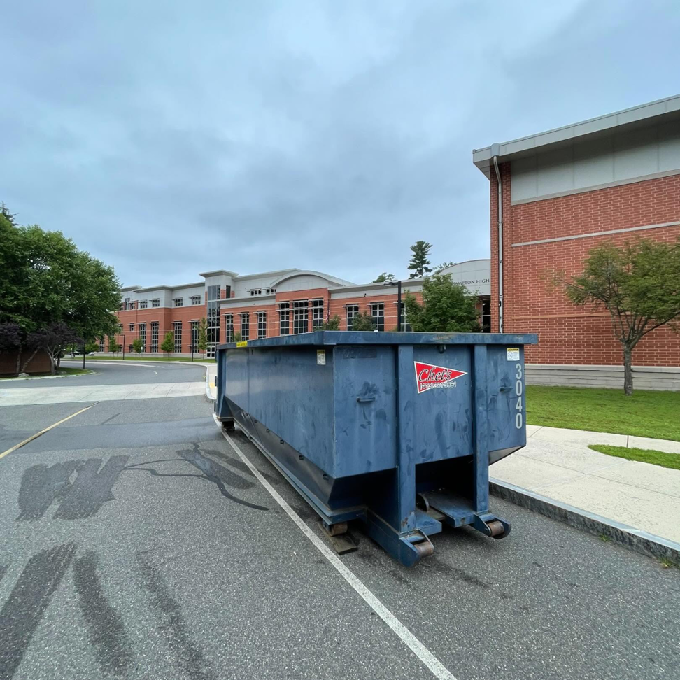 A blue roll-off dumpster from Chet's Disposal placed in front of a school building in Springfield, MA.