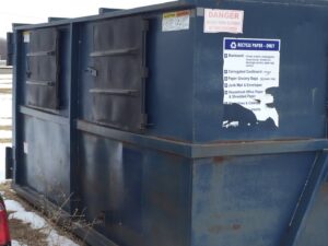 A blue recycling dumpster with a 'RECYCLE PAPER - ONLY' sign from NID Dumpster Rental in Nashua, IA.