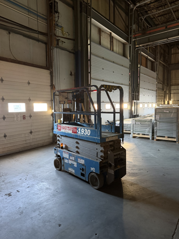 A blue scissor lift with Handyman branding inside a warehouse, rented from Handyman Rental in Portland, ME.