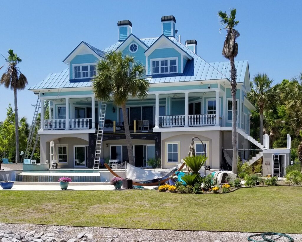 A large house with blue siding and a metal roof, showing exterior work by American Custom Exteriors in North Charleston, SC.
