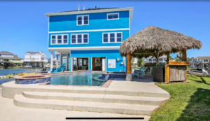 A blue waterfront home with a custom pool and tiki hut, showcasing work by Whitley Construction Services in Houston, TX.