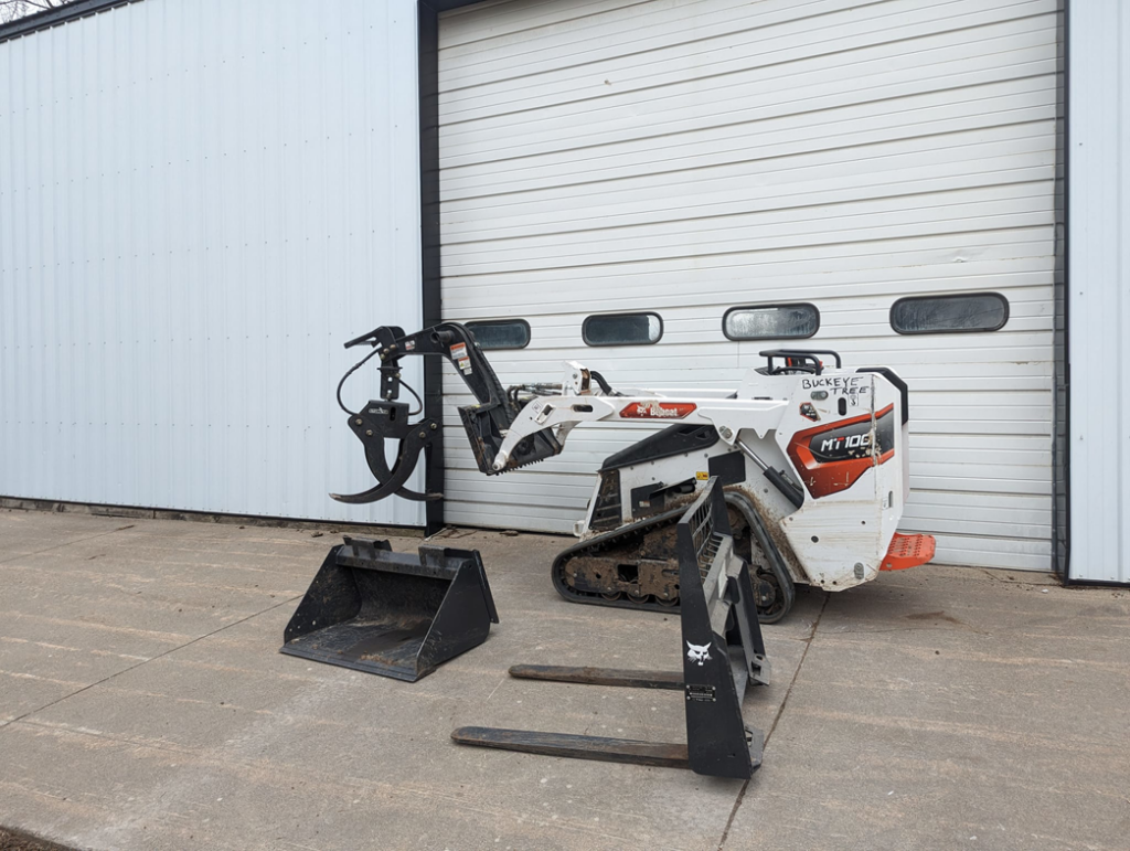 A Bobcat mini track loader with a grapple attachment, bucket, and pallet forks for tree service work at Buckeye Tree Services Inc. in Papillion, NE.