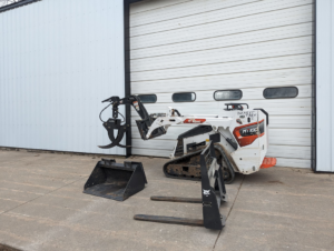 A Bobcat mini track loader with a grapple attachment, bucket, and pallet forks for tree service work at Buckeye Tree Services Inc. in Papillion, NE.